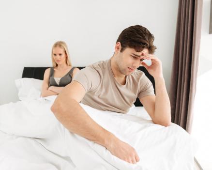 Проблемы в отношениях и ссора пары, сидящей на кровати в подавленном настроении.